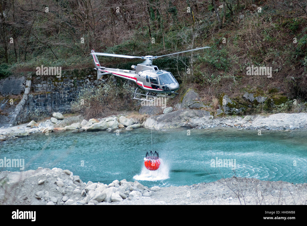 Fire Fighting elicottero raccolta di acqua in un secchio sospeso al di sotto del trinciatore da un fiume di montagna a dowse le fiamme Foto Stock