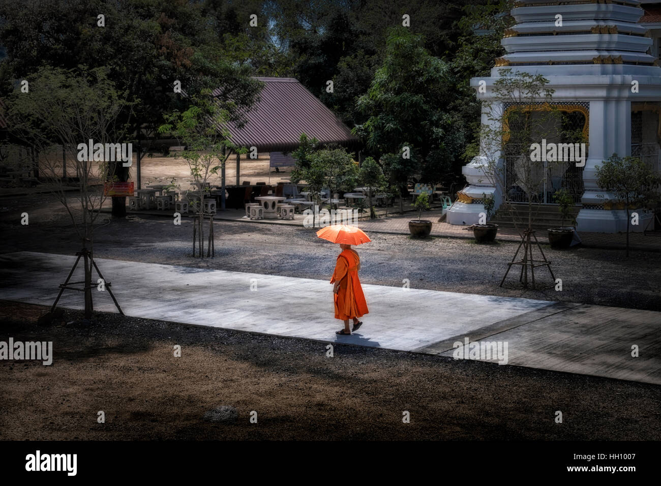 Monaco thailandese che cammina attraverso i giardini del tempio con un ombrello come ombrellone Foto Stock