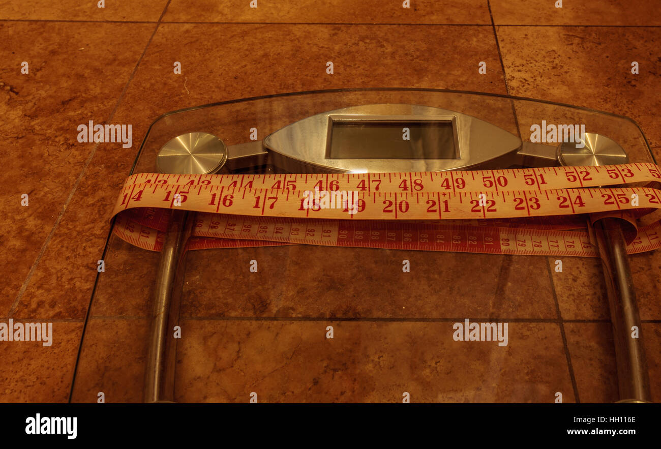 Scala per peso del monitor con un nastro di misurazione per prendere le misure per tenere traccia della forma fisica Foto Stock