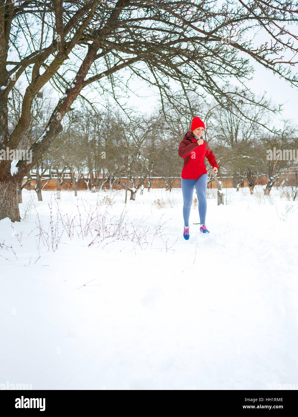 Sport donna acceso in inverno. Femminile ritratto in corpo pieno jogging nella neve sulla fredda giornata invernale Foto Stock