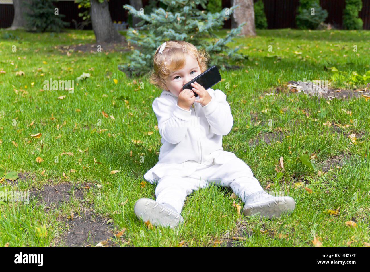 Carino bambina con telefono cellulare seduti su erba verde Foto Stock