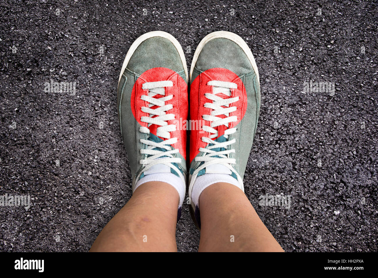Gambe con calzature sportive colorata con un cuore rosso, sullo sfondo di asfalto Foto Stock