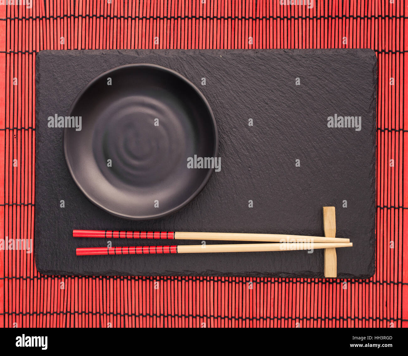 Bacchette e la piastra nera su ardesia coaster su red bamboo tappetino di scorrimento. In stile giapponese sfondo alimentare. Vista da sopra con lo spazio di copia Foto Stock