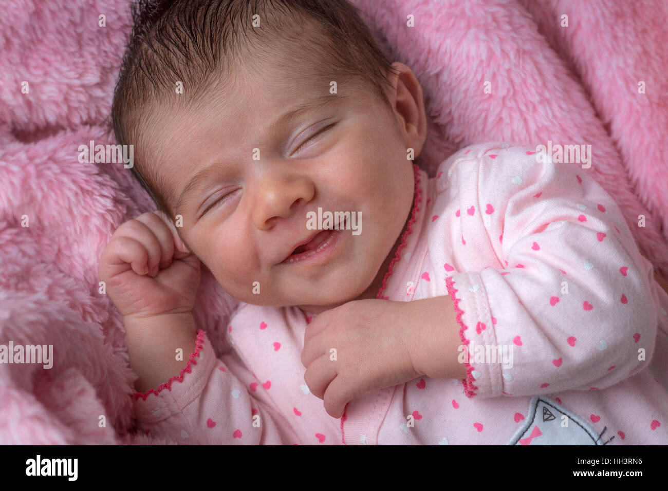 A meno di tre settimane di età sorridente bambina, sdraiato su una coperta rosa. Nouveau-né de moins de trois semaines souriant. Foto Stock