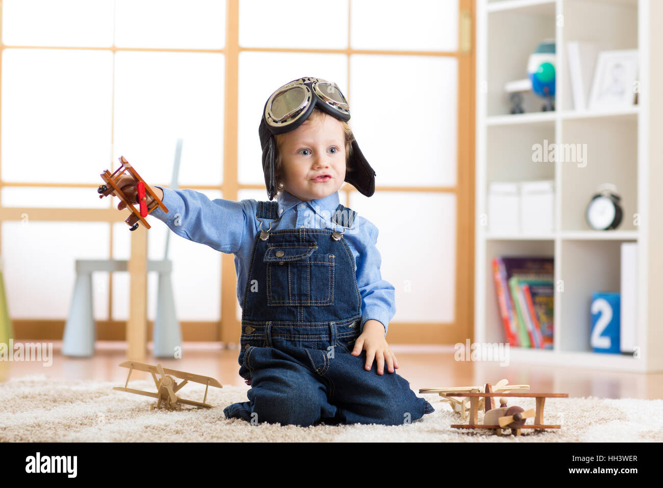 Bambino vestito come pilota aviatore gioca con un giocattolo aeroplani a casa nella sua stanza Foto Stock