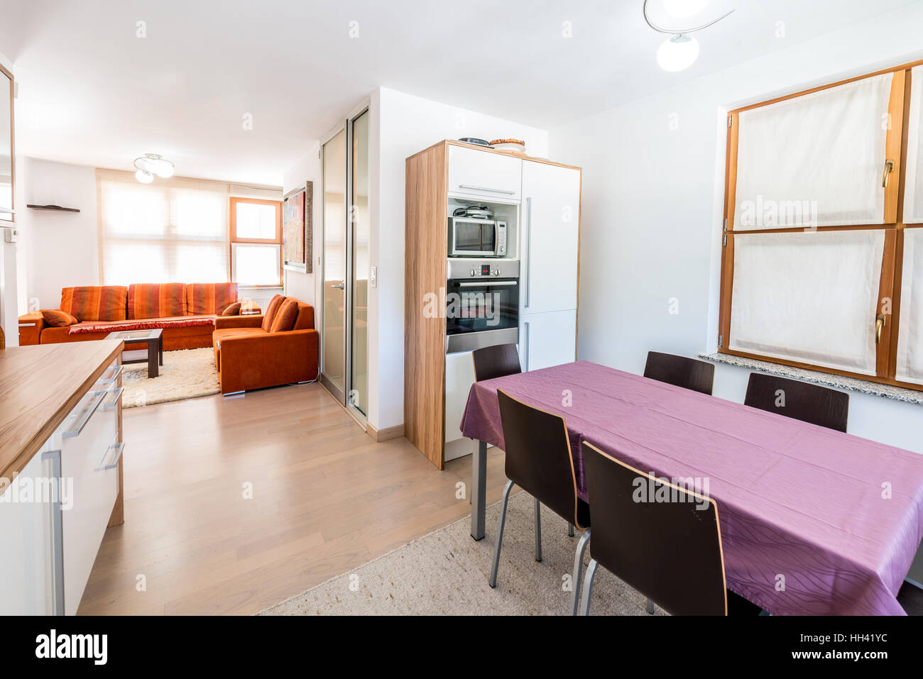 Moderna cucina open space con vista del soggiorno. Arredamento e tavolo da pranzo e tovaglia viola. Cucina in legno interni sala da pranzo un Foto Stock