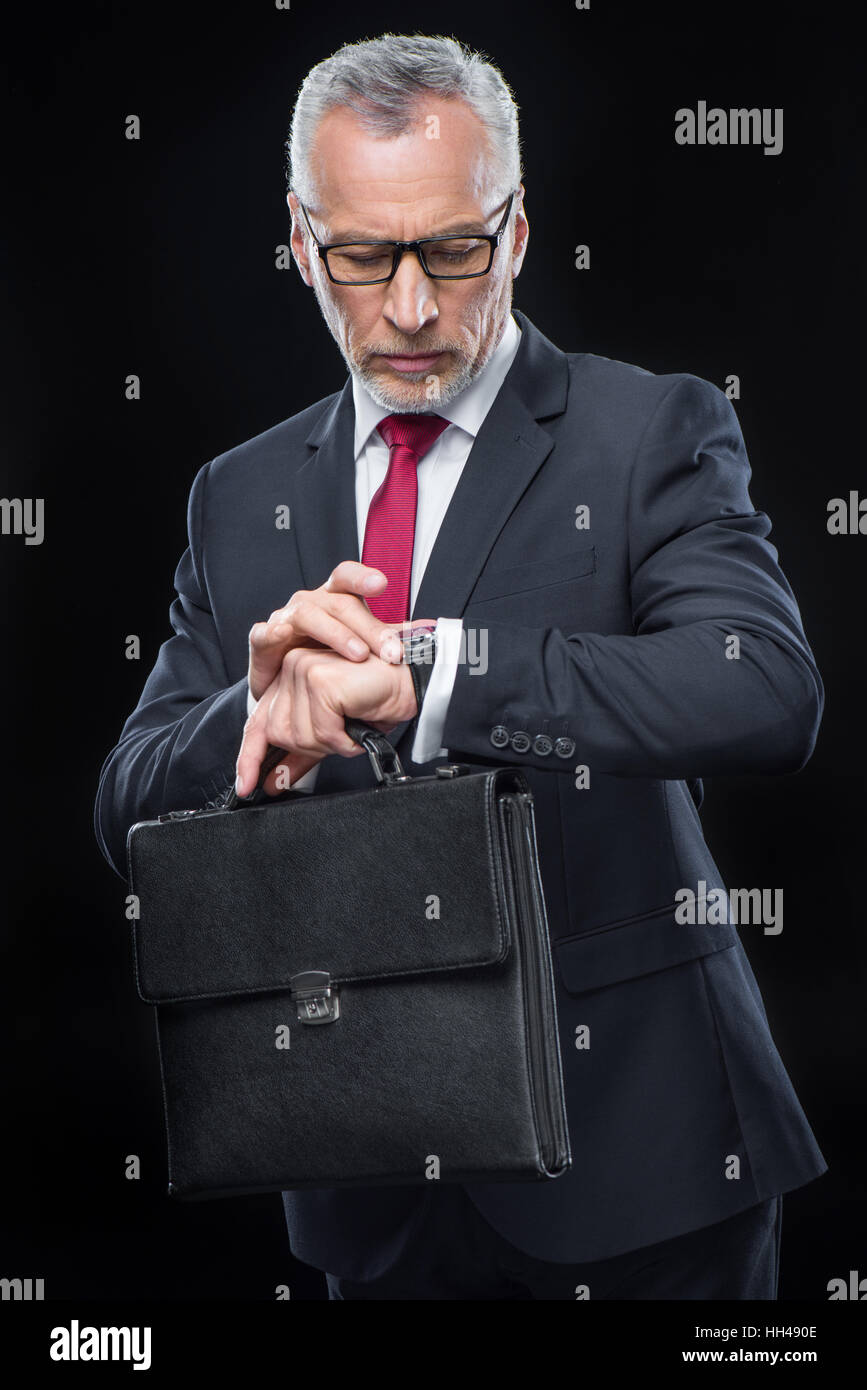 Imprenditore maturo valigetta di contenimento e guardando un orologio da polso Foto Stock