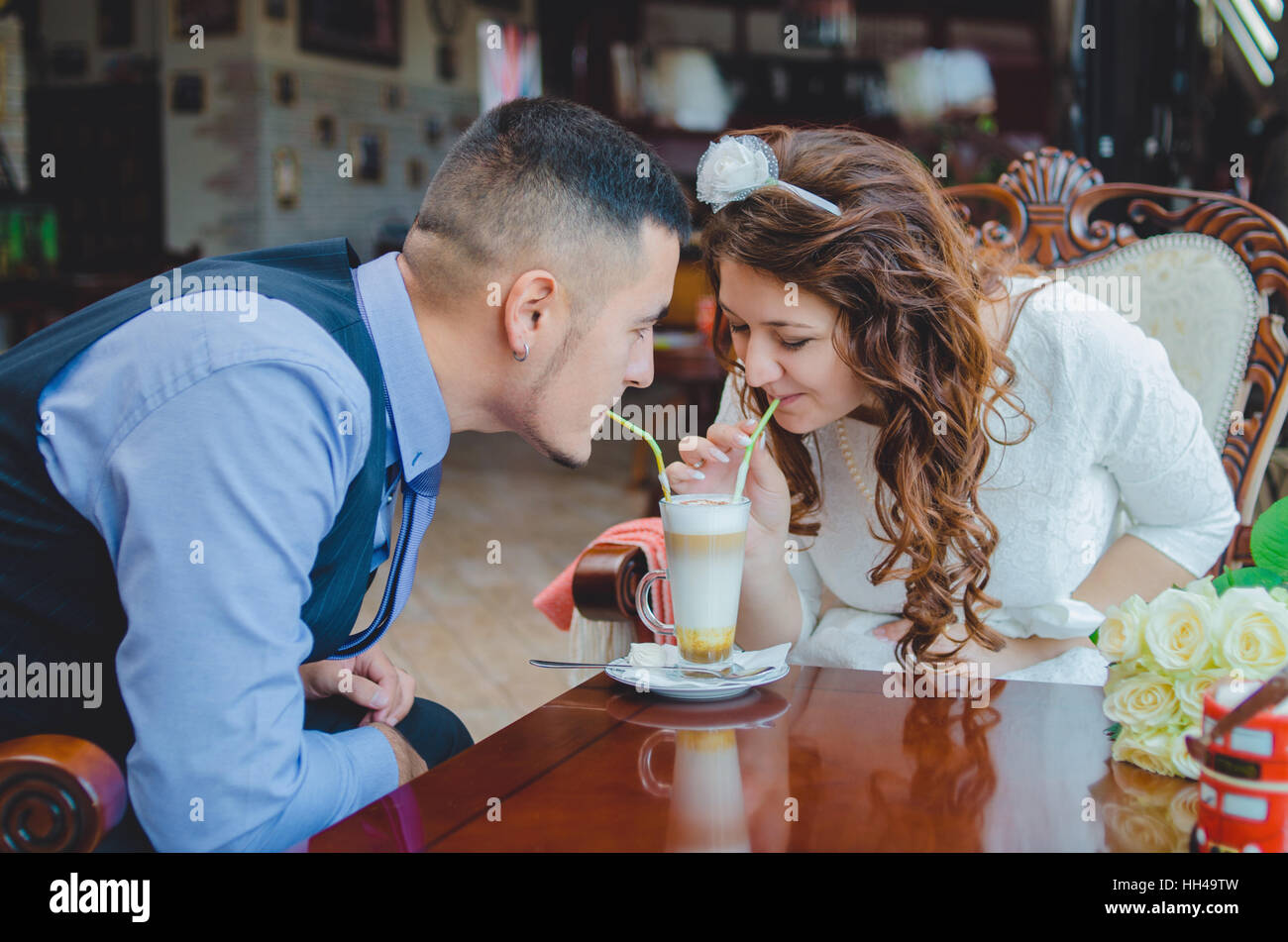 La giovane coppia amorevole beve un cappuccino da un vetro attraverso tubuli. Nozze Foto Stock