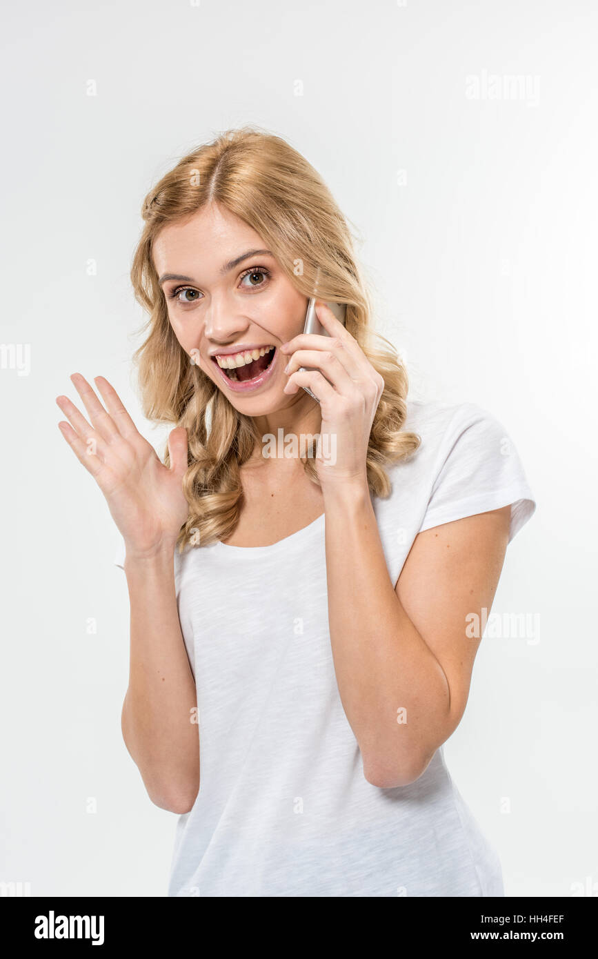 Excited donna giovane utilizza lo smartphone e guardando la telecamera su bianco Foto Stock