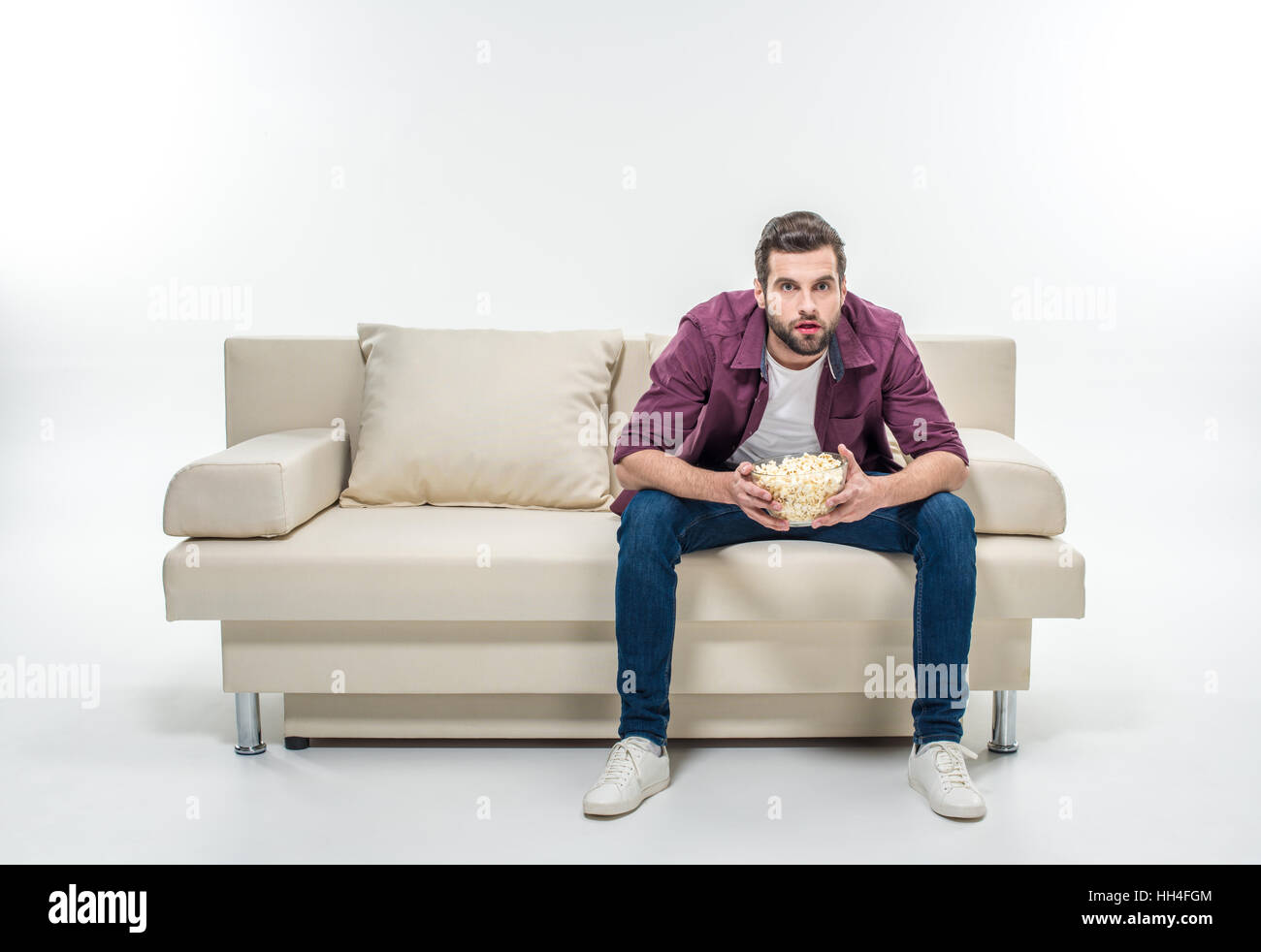 Concentrato giovane uomo seduto sul divano con pop-corn Foto Stock