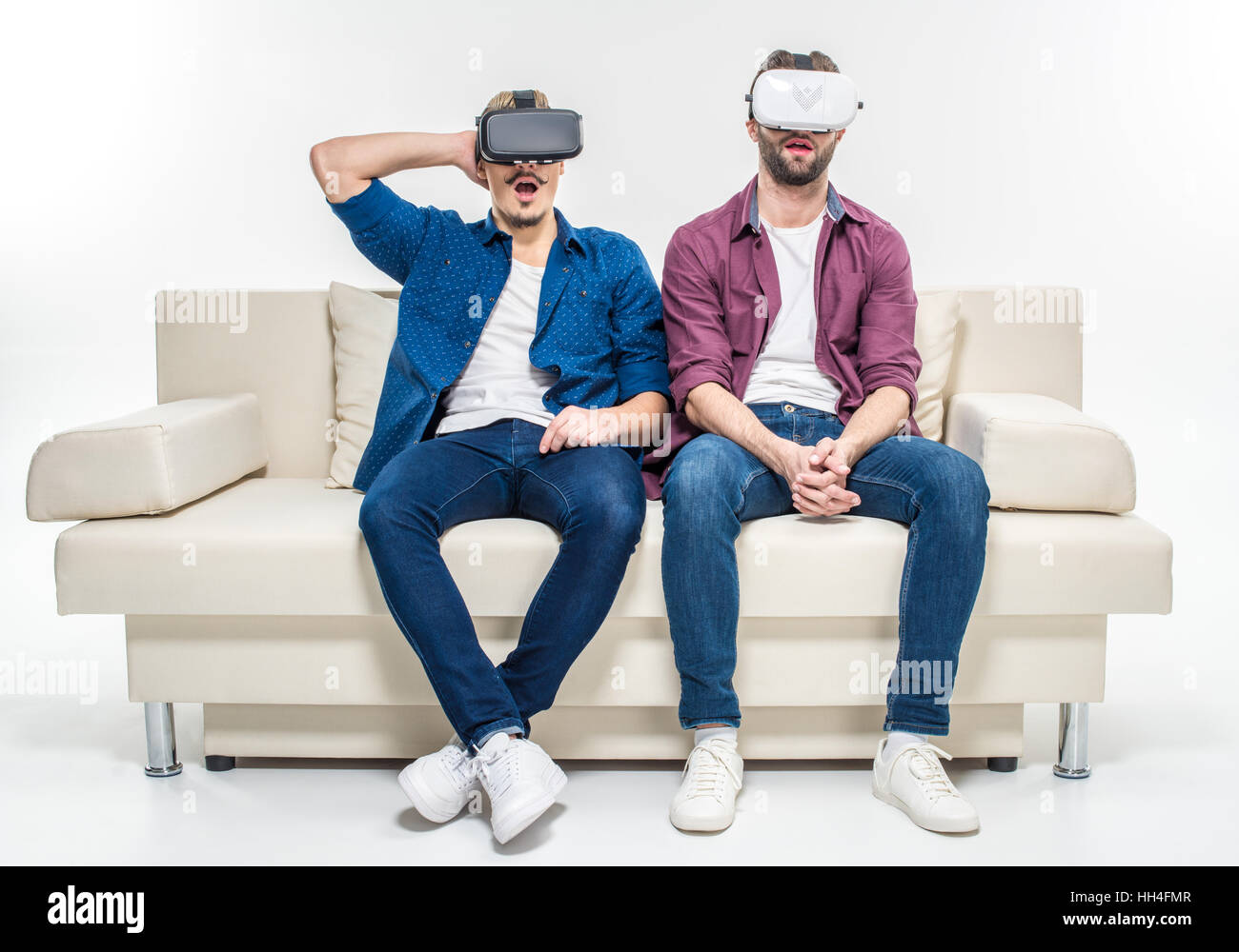 Amici di sesso maschile seduto sul divano bianco in realtà virtuale di cuffie Foto Stock