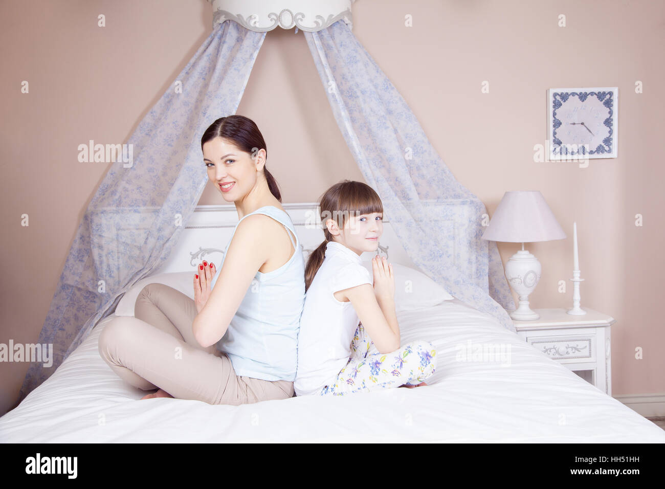 Felice madre e figlia meditando e sorridere mentre in seduta yoga pone sul letto di casa. Studio shot. Foto Stock