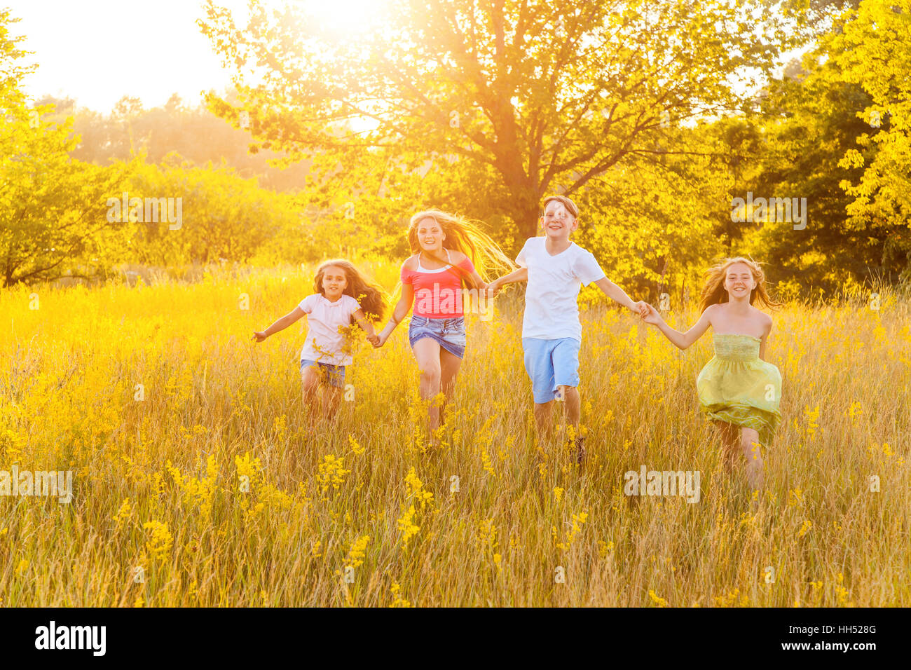 Felice quattro bellissimi bambini esegue la riproduzione in movimento insieme nella bella giornata d'estate. jumping e guardando la fotocamera. Foto Stock