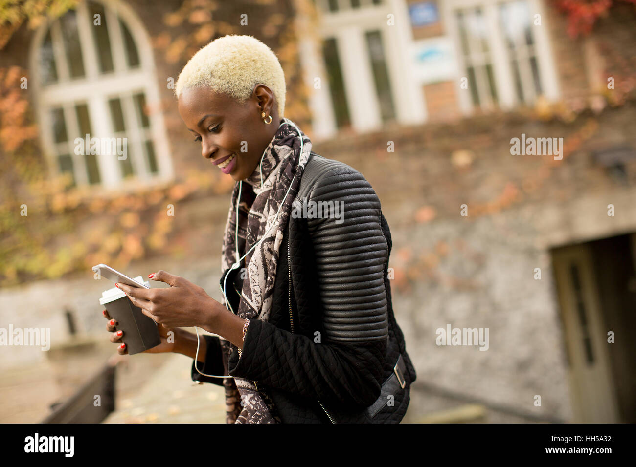 Accattivante americano africano donna con il telefono cellulare e la tazza di caffè in autunno park Foto Stock