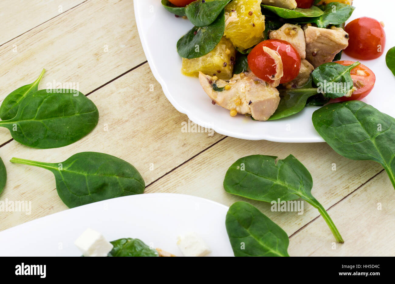 Guarnito con taglio feta insalata di spinaci, pollo, pomodori ciliegini e arancione sulla piastra bianca Foto Stock