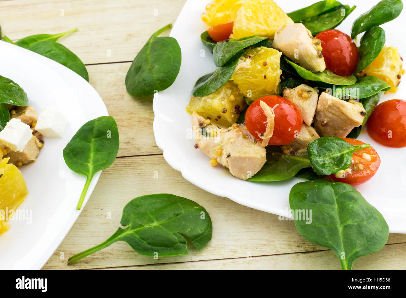 Guarnito con taglio feta insalata di spinaci, pollo, pomodori ciliegini e arancione sulla piastra bianca Foto Stock