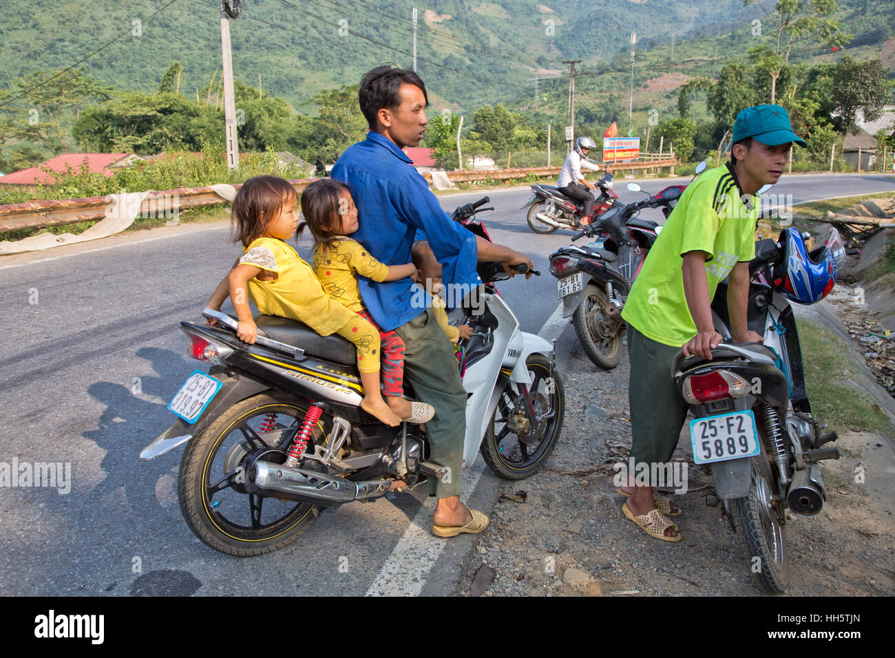 Padre il trasporto di tre bambini, fermo lungo la strada rurale, avente una conversazione dal mercato degli agricoltori, Yamaha Sirius RC motociclo. Foto Stock
