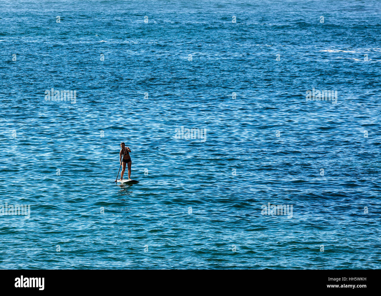 Lone giovane donna paddle imbarco sul mare liscio lontano dalla riva Foto Stock