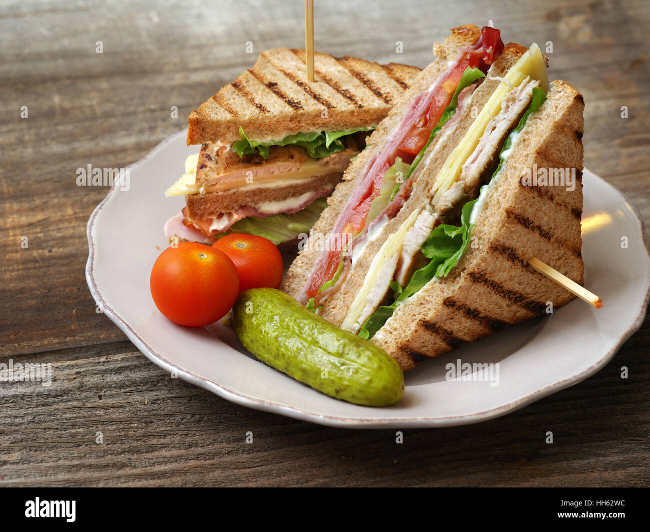 Foto di un club sandwich realizzati con la Turchia, pancetta, prosciutto, pomodoro, formaggio, lattuga e guarnito con una salamoia e due pomodori ciliegia. Foto Stock