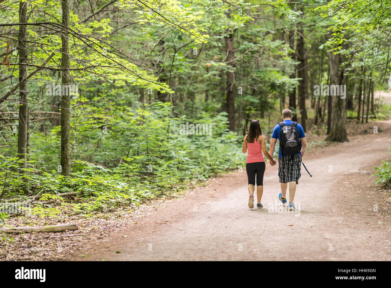 Paio di persone escursionismo insieme nel bosco verso il basso un percorso sterrato su una bella giornata d'estate. Baldacchino verde di alberi al di sopra di essi. Vista dal retro del PERS Foto Stock