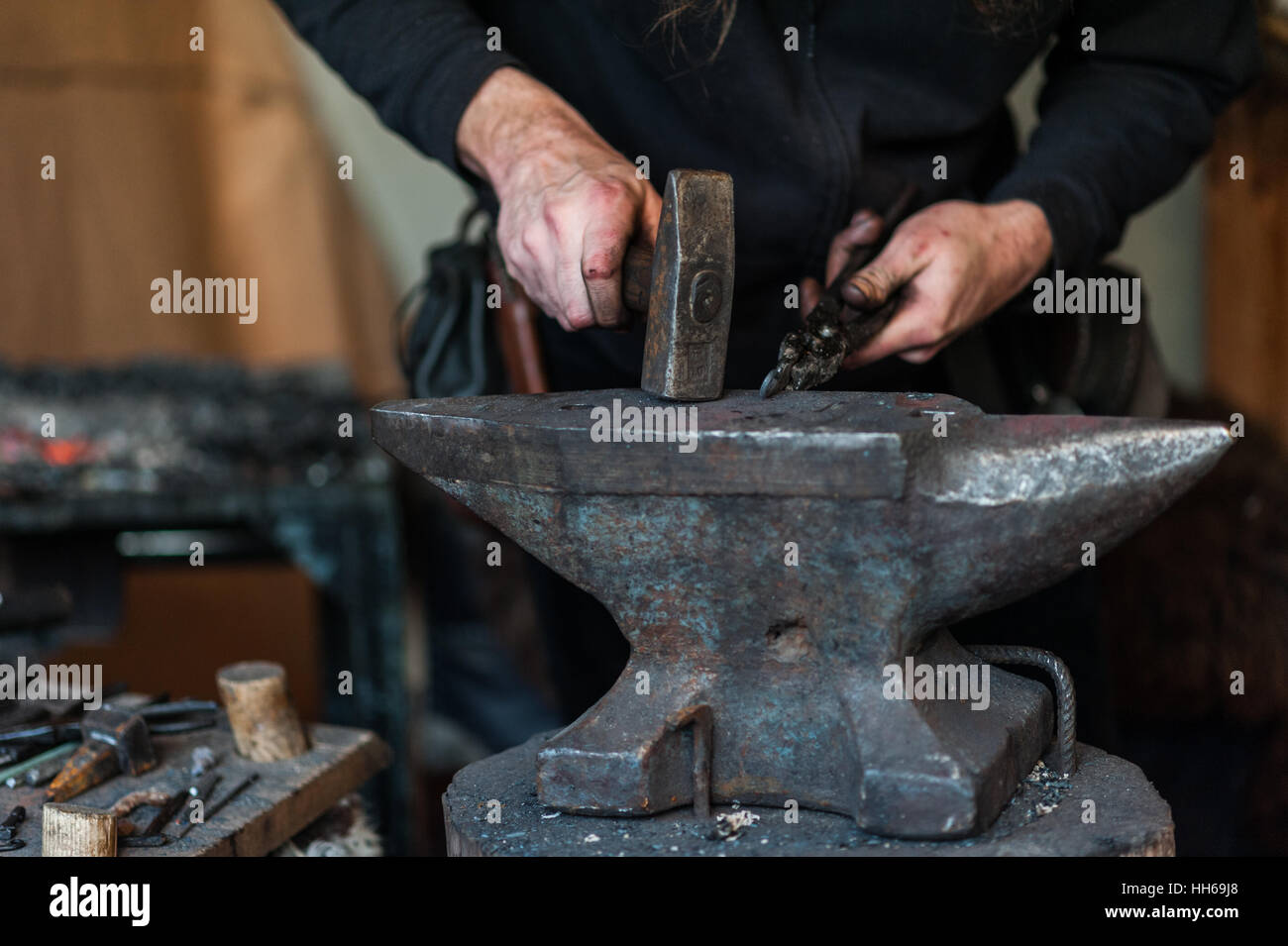 Fabbro in officina. La lavorazione dei metalli con martello e strumenti sull'incudine nel forge. Foto Stock