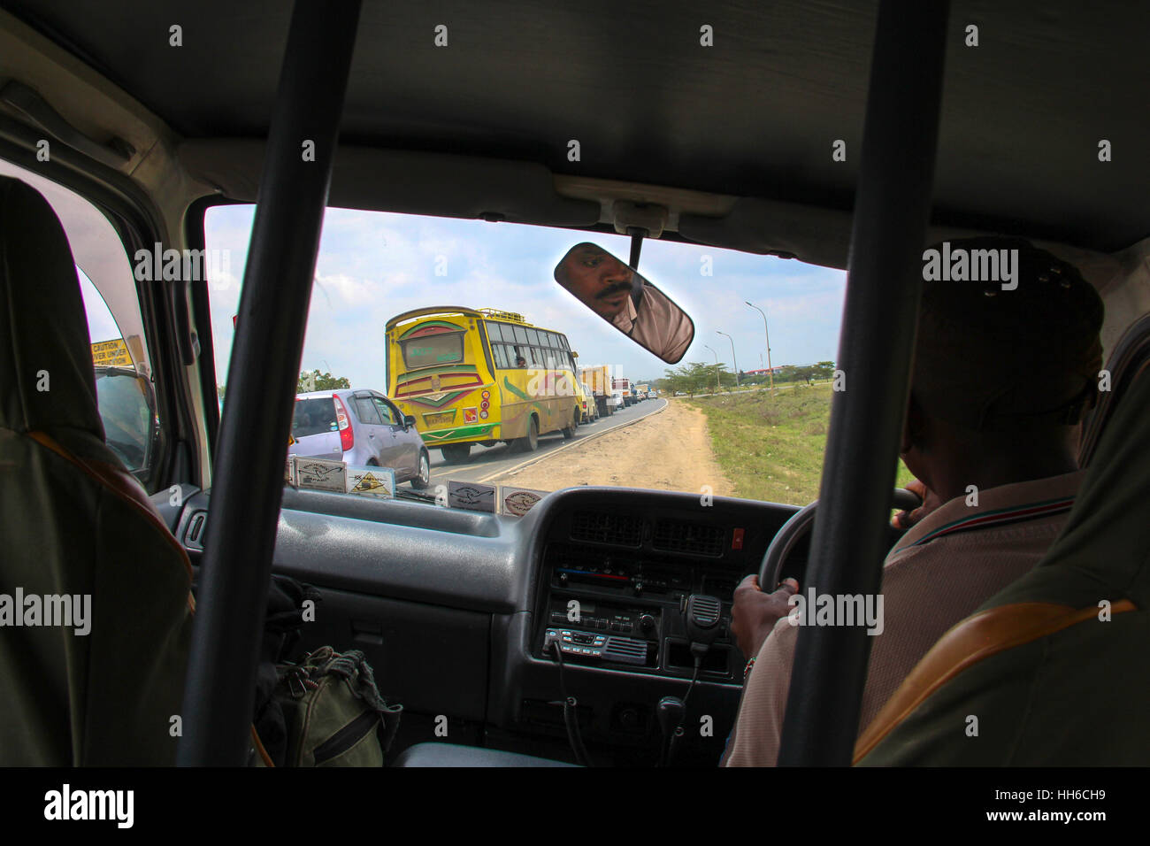 Vista dal sedile posteriore di un furgone di safari mentre evitando traffico difettoso a Nairobi (Kenya) con il viso del conducente si vede nello specchietto retrovisore Foto Stock