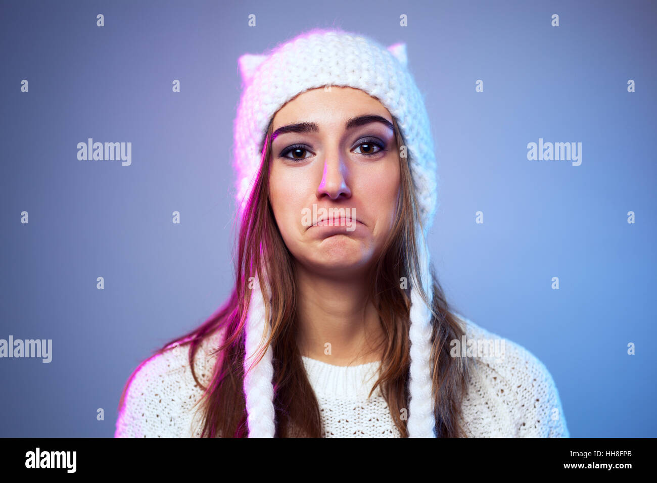 Giovane donna triste nel caldo inverno abbigliamento in bianco su sfondo blu Foto Stock
