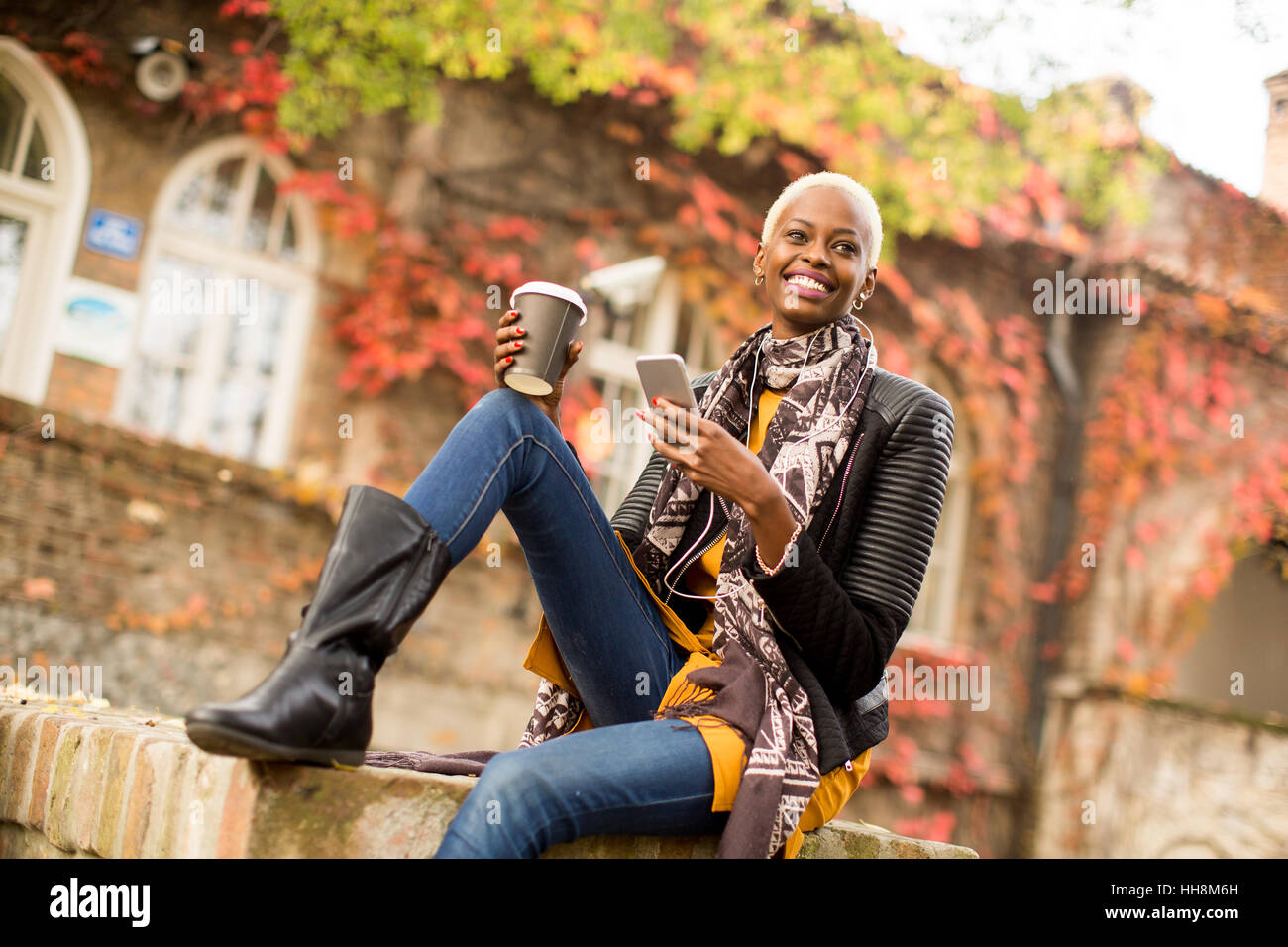 Accattivante americano africano donna con il telefono cellulare e la tazza di caffè in autunno park Foto Stock