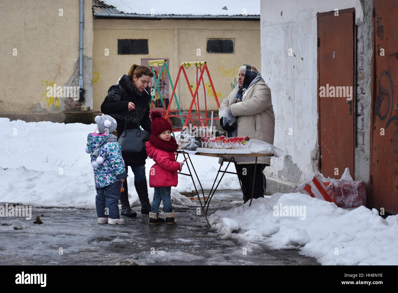 Giovane madre di lecca-lecca di acquisto per i suoi due bambini piccoli da una vecchia signora nella scuola del villaggio cantiere durante la celebrazione Surva Foto Stock