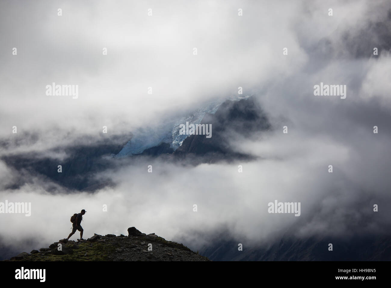 Stagliano uomo escursionismo su un crinale sotto le nuvole Aoraki nel Parco nazionale di Mount Cook in Nuova Zelanda Foto Stock