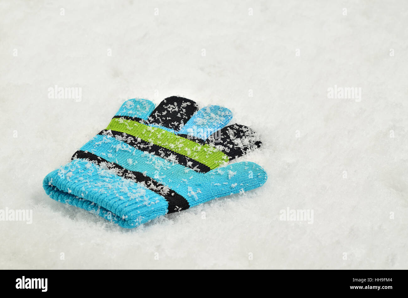 Close up di un singolo, perso un guanto, ciano, verde chiaro e nero a strisce e coperte di neve,su sfondo di neve Foto Stock