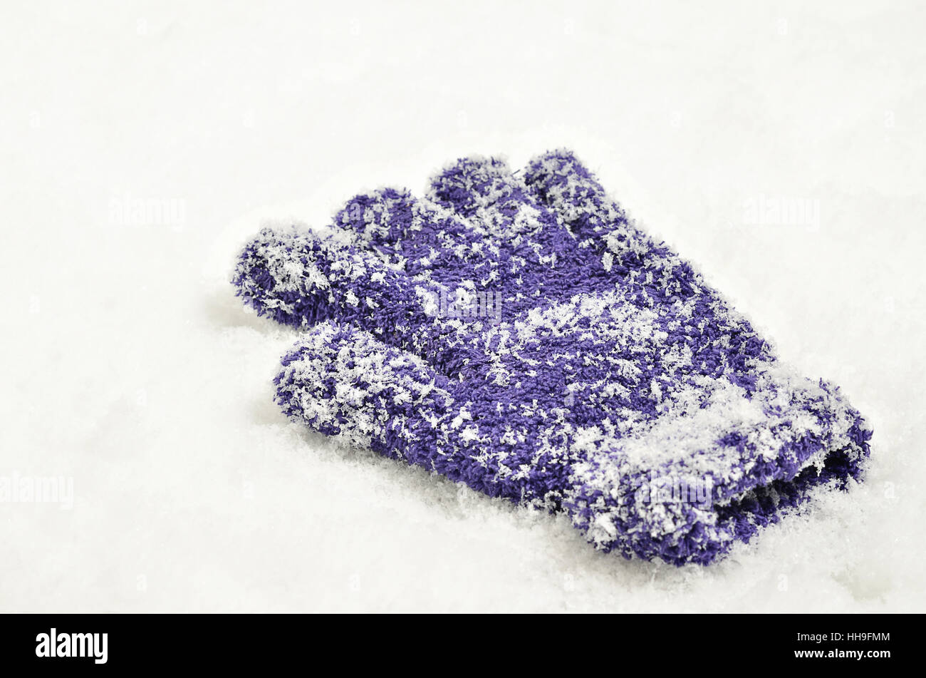 Close up di un singolo, perso guanto, viola, viola o lilla e coperto di neve su sfondo di neve Foto Stock