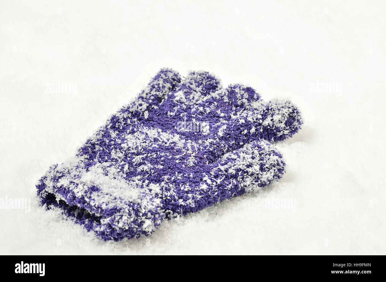 Close up di un singolo, perso guanto, viola, viola o lilla e ricoperta di neve su sfondo di neve Foto Stock