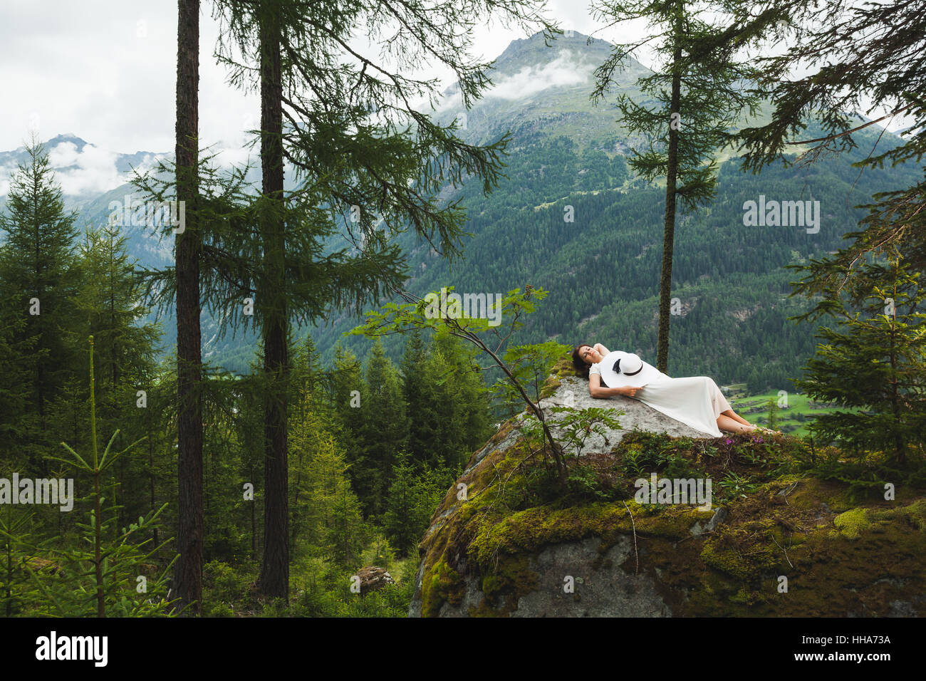 Giovane donna in abito bianco e hat posa su pietra in montagna Foto Stock