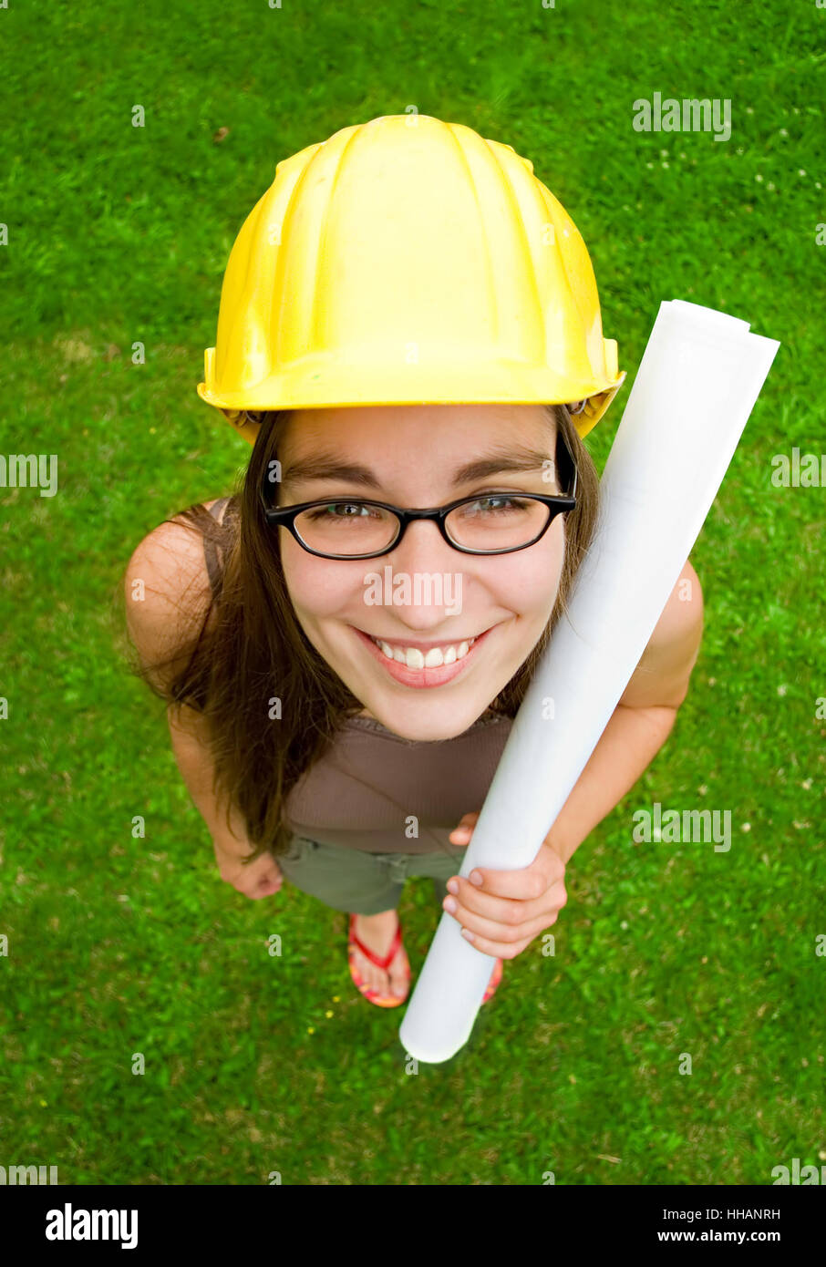 Giovane donna sorridente architetto o builder indossando un giallo hart hat holding piani architettonici Foto Stock