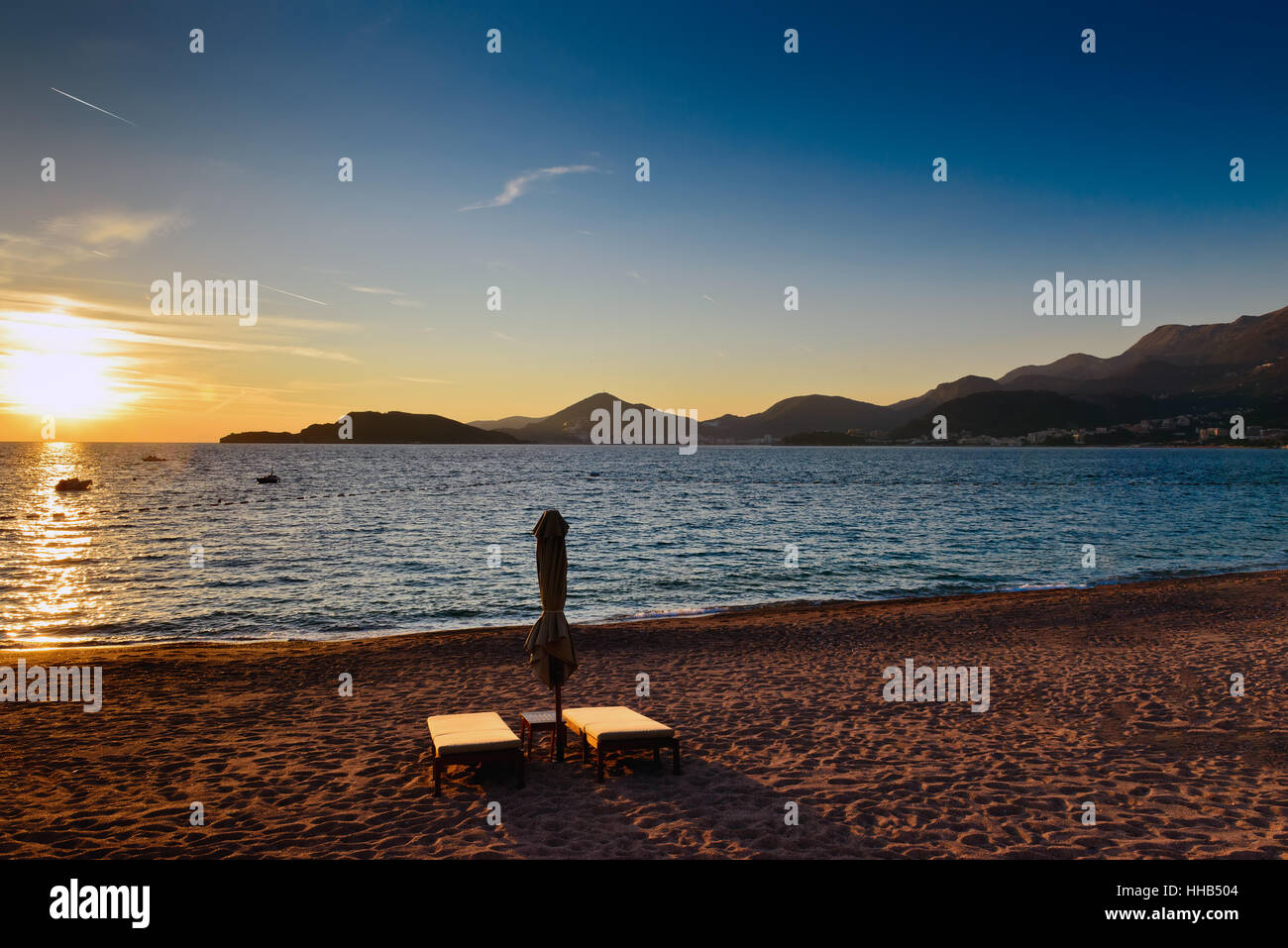 Sveti Stefan spiaggia di sabbia con un paio di sdraio vicino a Budva, Montenegro. Balcani, mare Adriatico, l'Europa. Tramonto Foto Stock