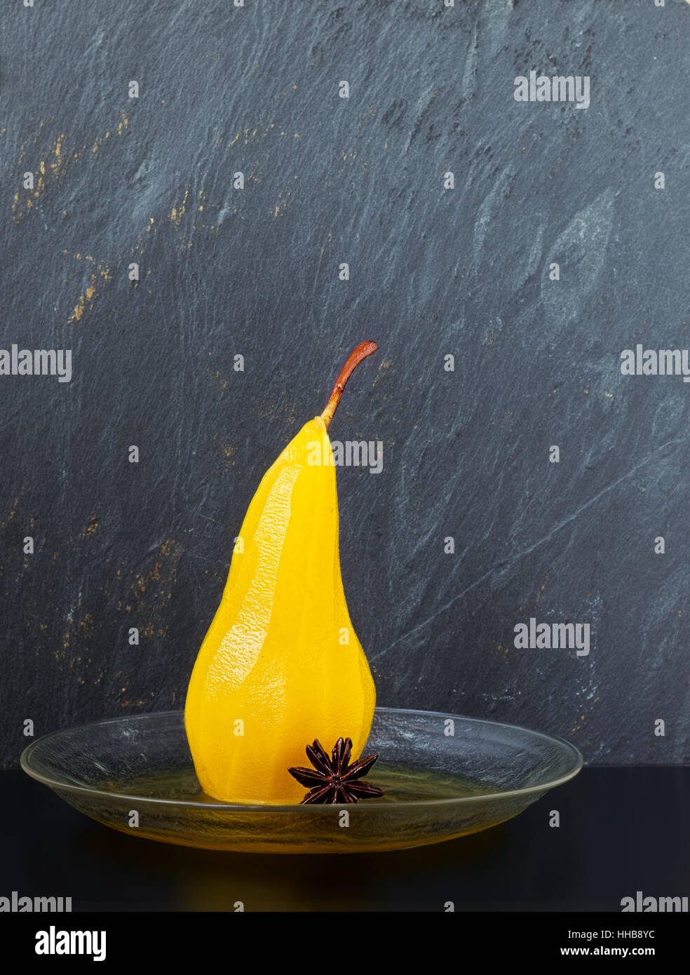 Singola pera affogata in zucchero e sciroppo di zafferano conditi con anice stellato su una lastra di vetro con un grigio Sfondo ardesia Foto Stock