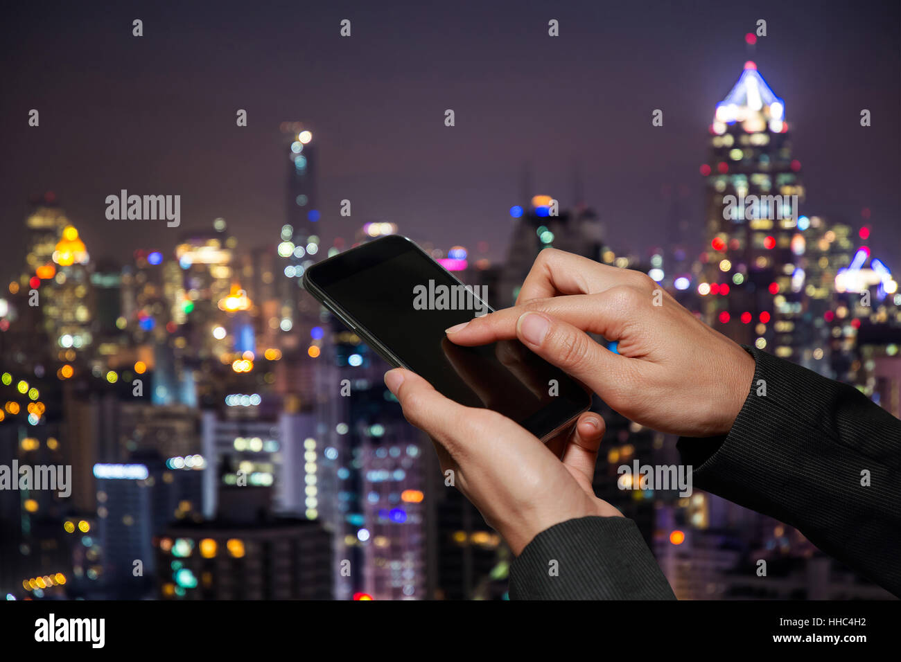 Donna tenere in mano e il touch screen smart phone, cellphone su abstract sfocata la notte sullo sfondo della città. Foto Stock