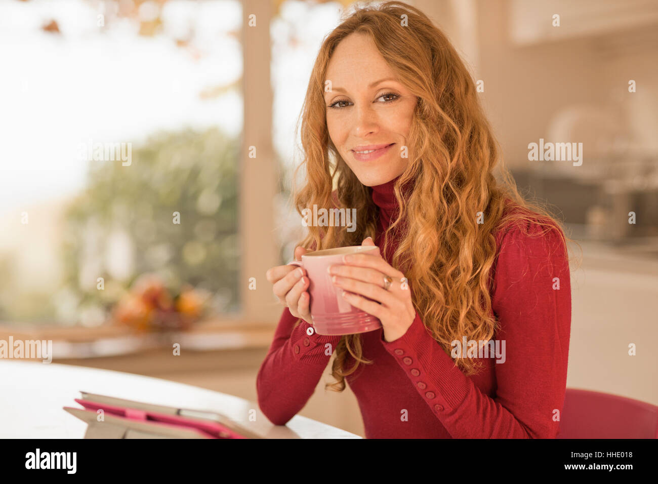Ritratto di donna sorridente a bere caffè e con tavoletta digitale in cucina Foto Stock