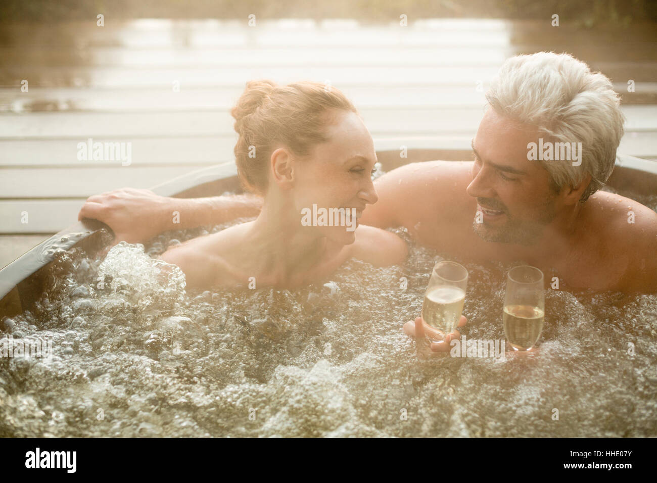 Coppia sorridente bevendo champagne in ammollo nella vasca calda sul patio Foto Stock
