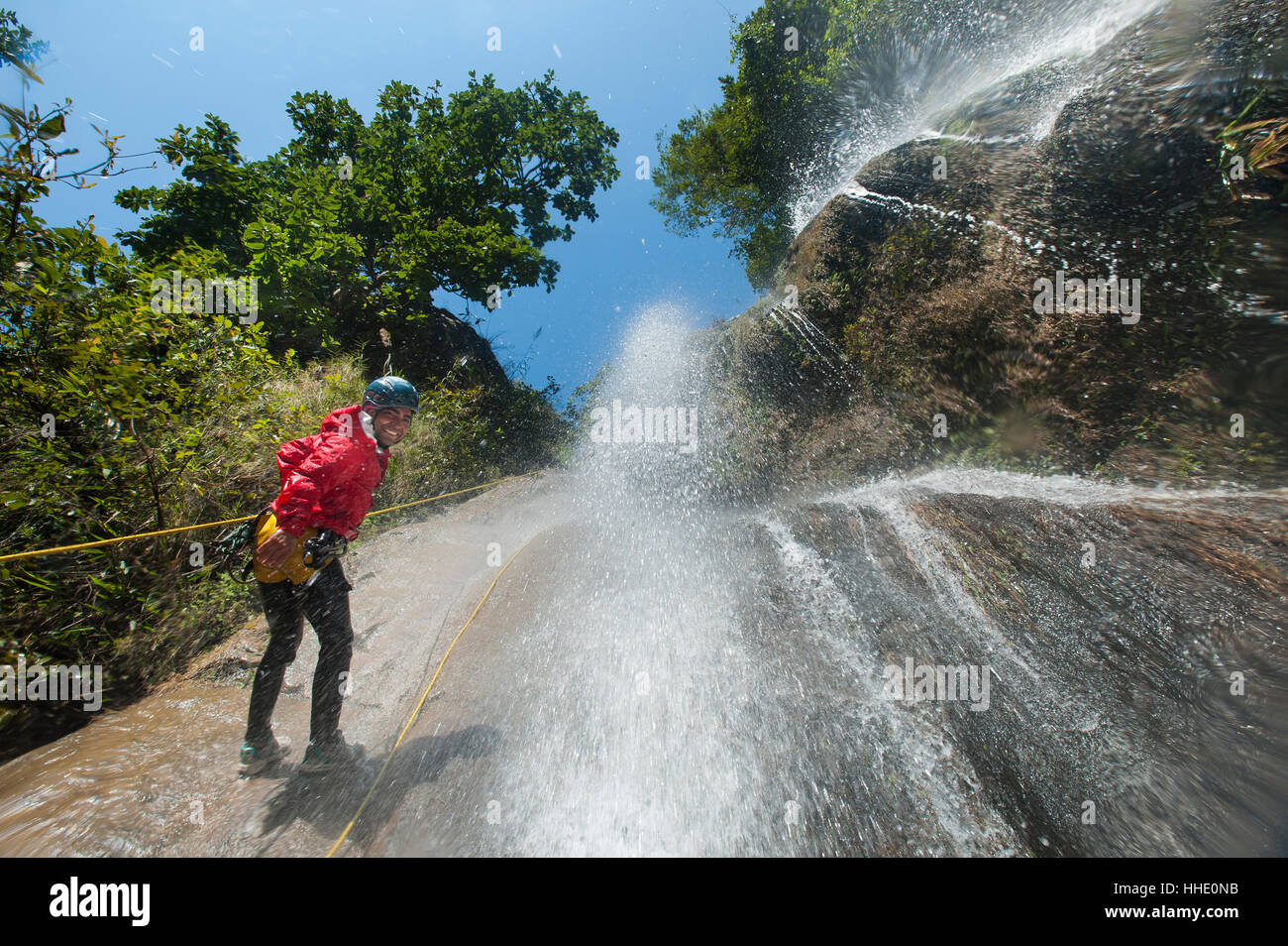 Un uomo si sofferma a sorridere per la fotocamera mentre il canyoning in una cascata, Nepal Foto Stock