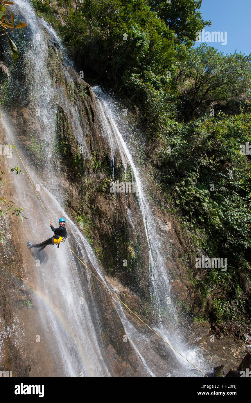 Una ragazza si sofferma a sorridere per la fotocamera mentre il canyoning in una cascata, Nepal Foto Stock