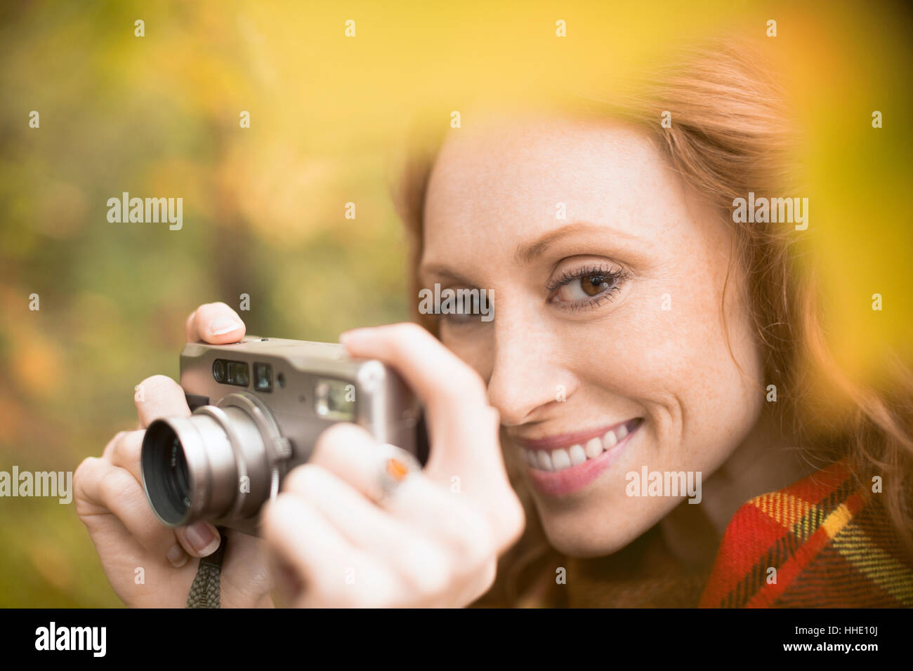 Close up donna sorridente utilizzando una fotocamera digitale tra foglie di autunno Foto Stock