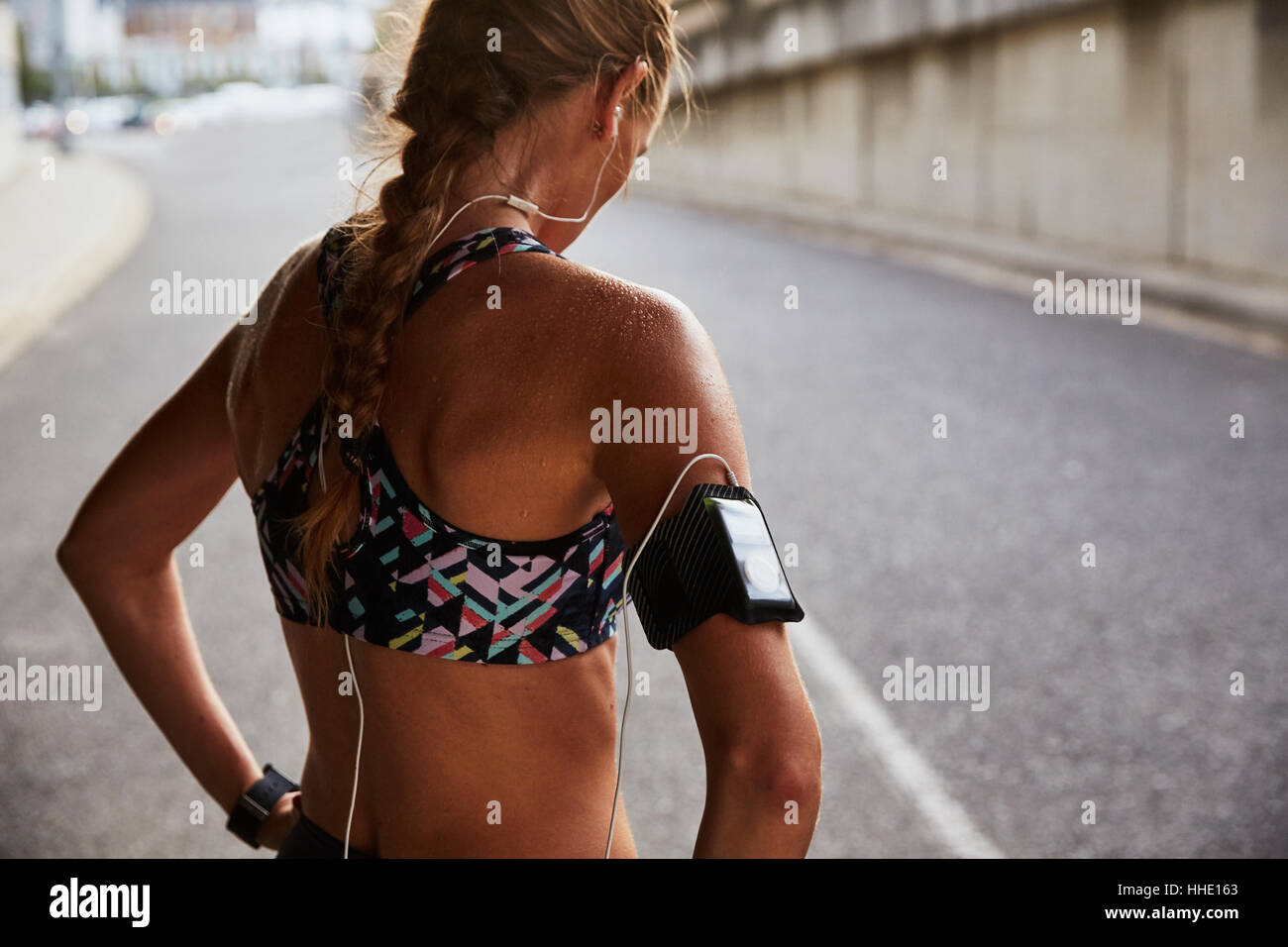 Montare femminile nel reggiseno per lo sport con lettore mp3 fascia da braccio e cuffia in appoggio sulla strada urbana Foto Stock