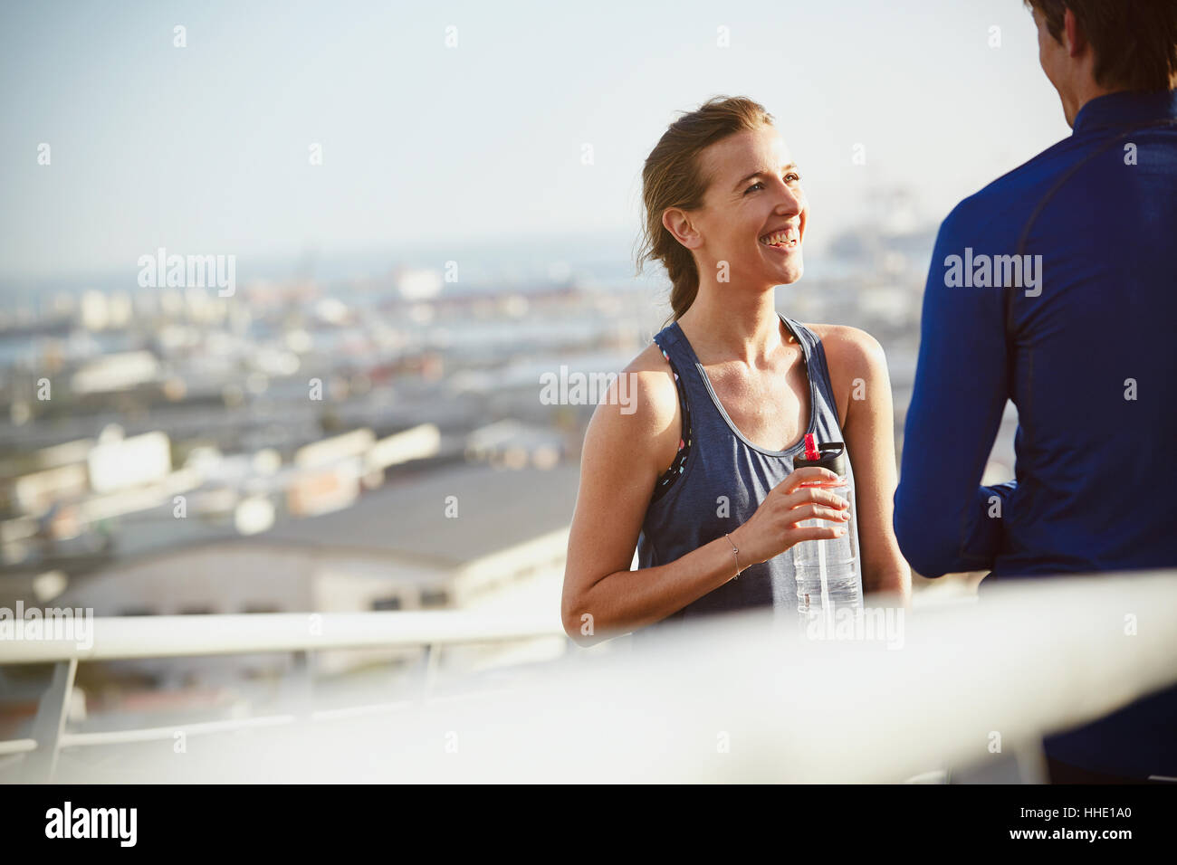 Sorridente runner matura in appoggio acqua potabile sulla soleggiata passerella urbana Foto Stock