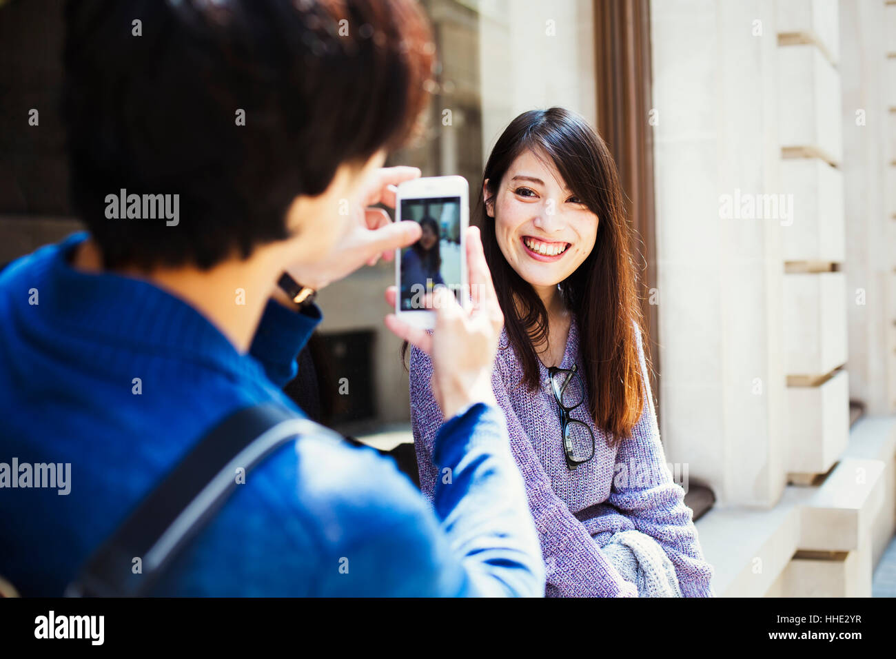 Un giovane giapponese l uomo e la donna godendo una giornata fuori a Londra, in piedi su un marciapiede, scattare una foto. Foto Stock