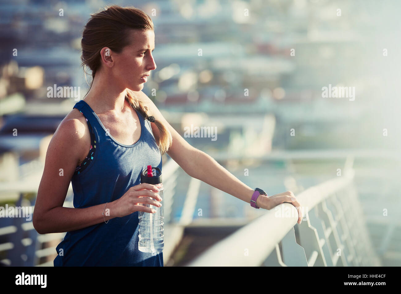Femmina con runner di acqua in bottiglia in appoggio sulla soleggiata passerella urbana Foto Stock
