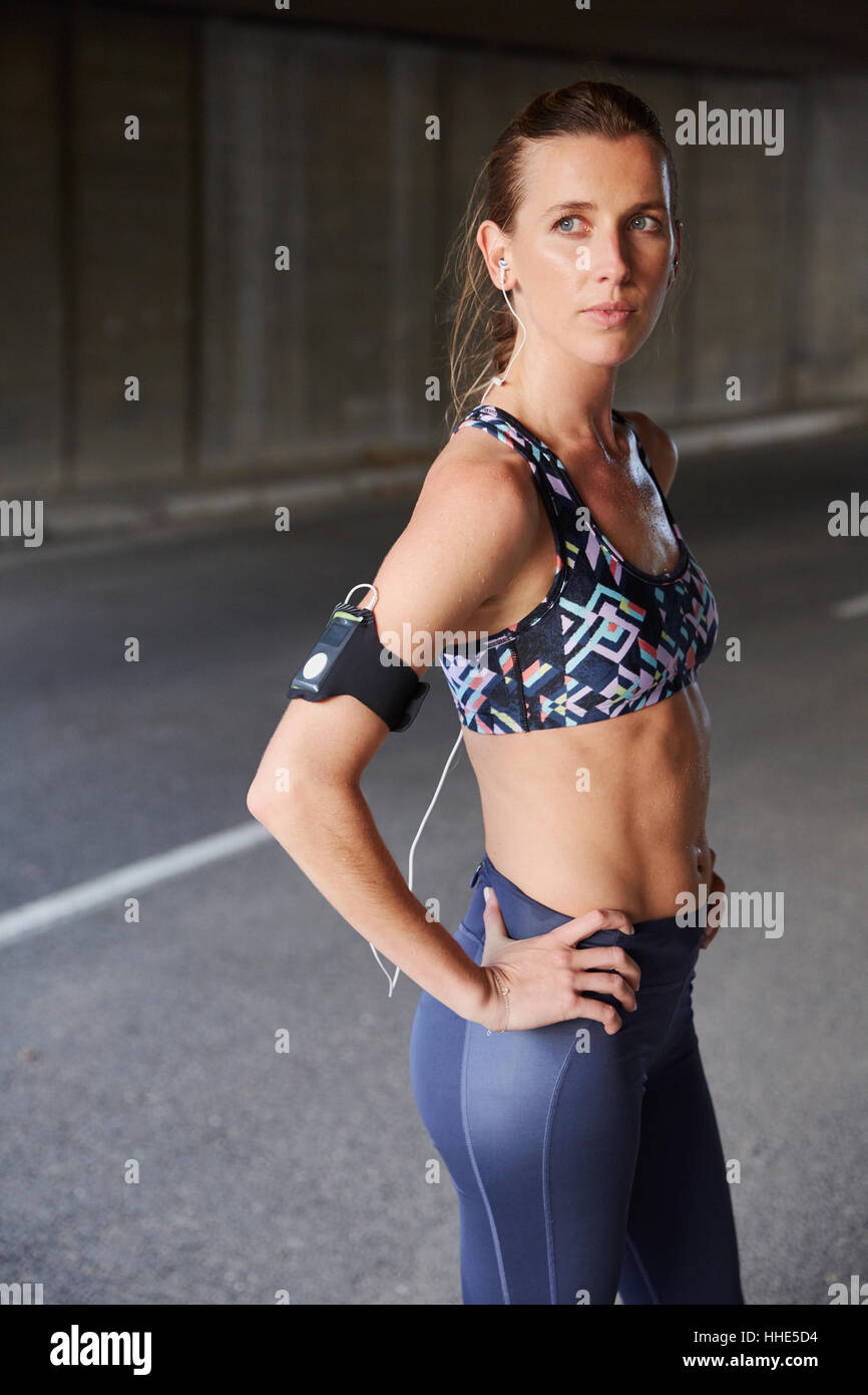 Montare gravi femminile nel reggiseno per lo sport con lettore mp3 fascia da braccio e cuffia su strada urbana Foto Stock