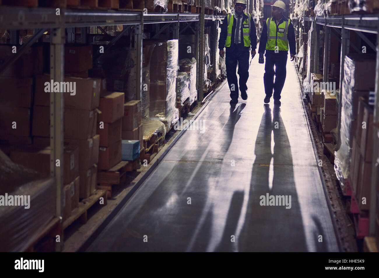 Lavoratori a piedi lungo la merce sugli scaffali della distribuzione corridoio magazzino Foto Stock