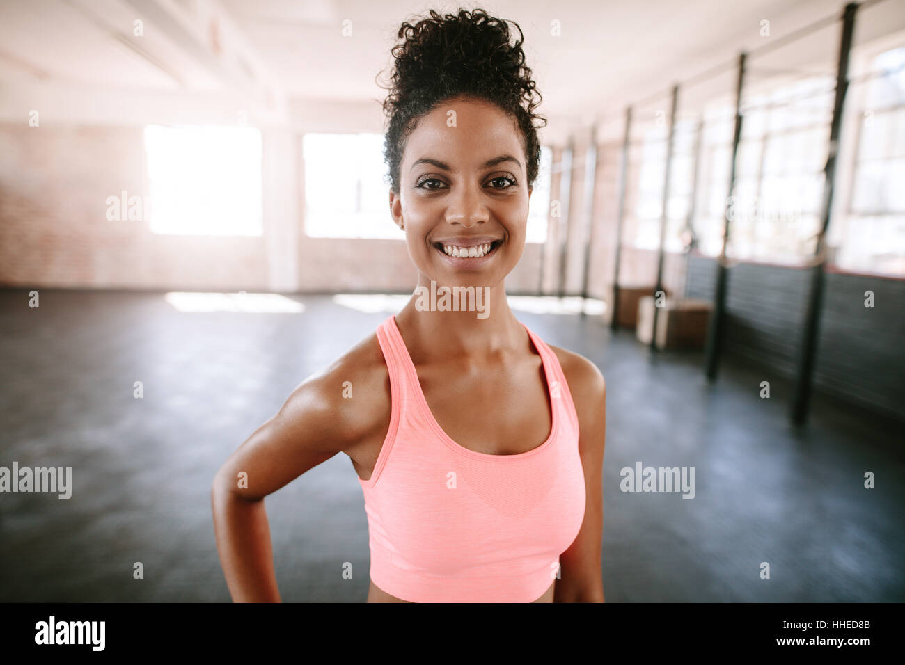 Ritratto della forma e bella donna africana in piedi in palestra. modello di fitness in sportsbra che sorride alla fotocamera. Foto Stock